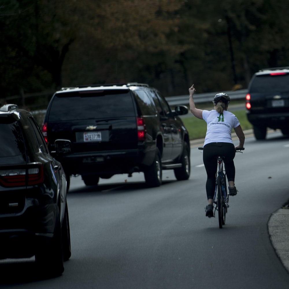 Juli Briskman, à vélo, levant son majeur au moment où passe le convoi du président Trump.
