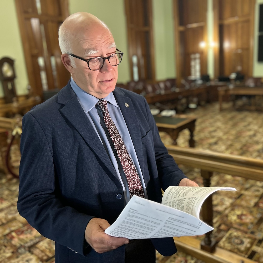 Une photo de David Coon, dans la salle de comité, tenant dans ses mains son projet de loi. 