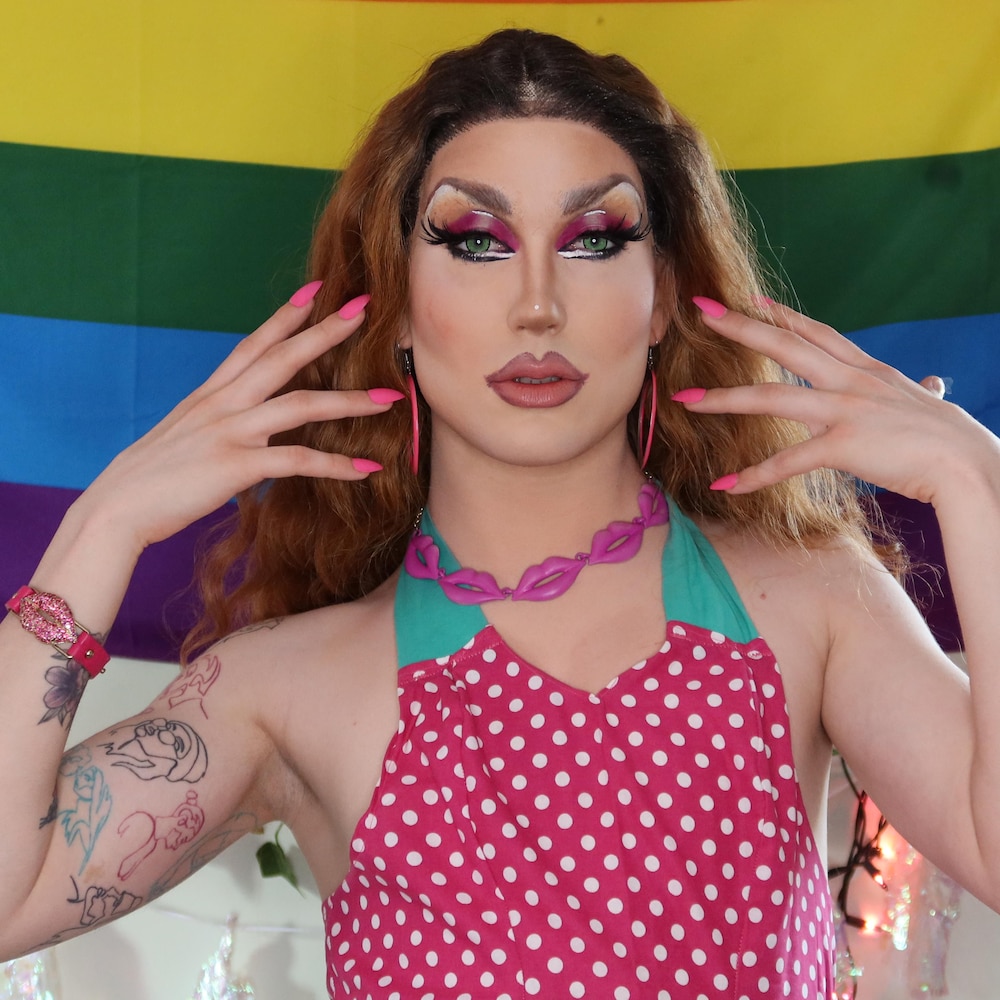 Debbie Fluid pose devant un drapeau de la fierté gaie.