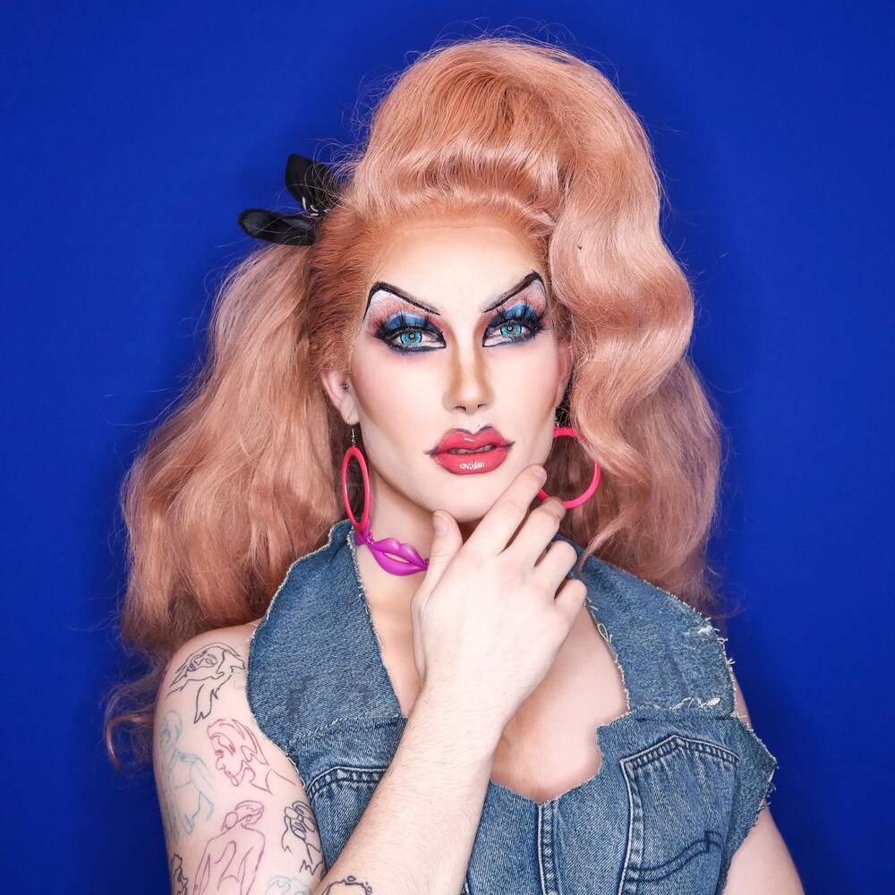 Debbie Fluid pose devant un fond bleu, habillée d'une veste de jeans.