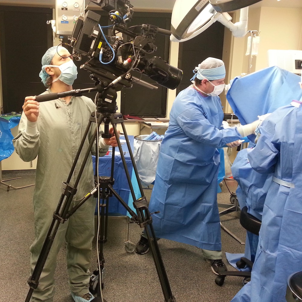 Cameramen filme des chirurgiens masqués et gantés.