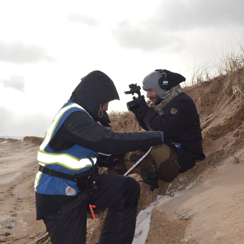 Deux personnes filment et prennent des mesures sur une dune de sable.