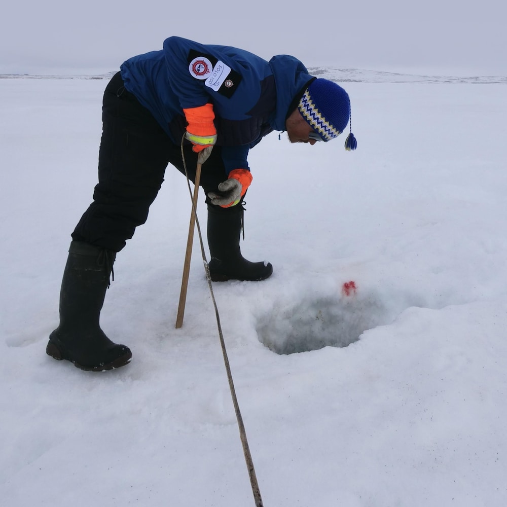 Devon Malik en train de regarder dans un trou de pêche sur la banquise, au mois de juin à Resolute Bay, dans le nord du Nunavut.
