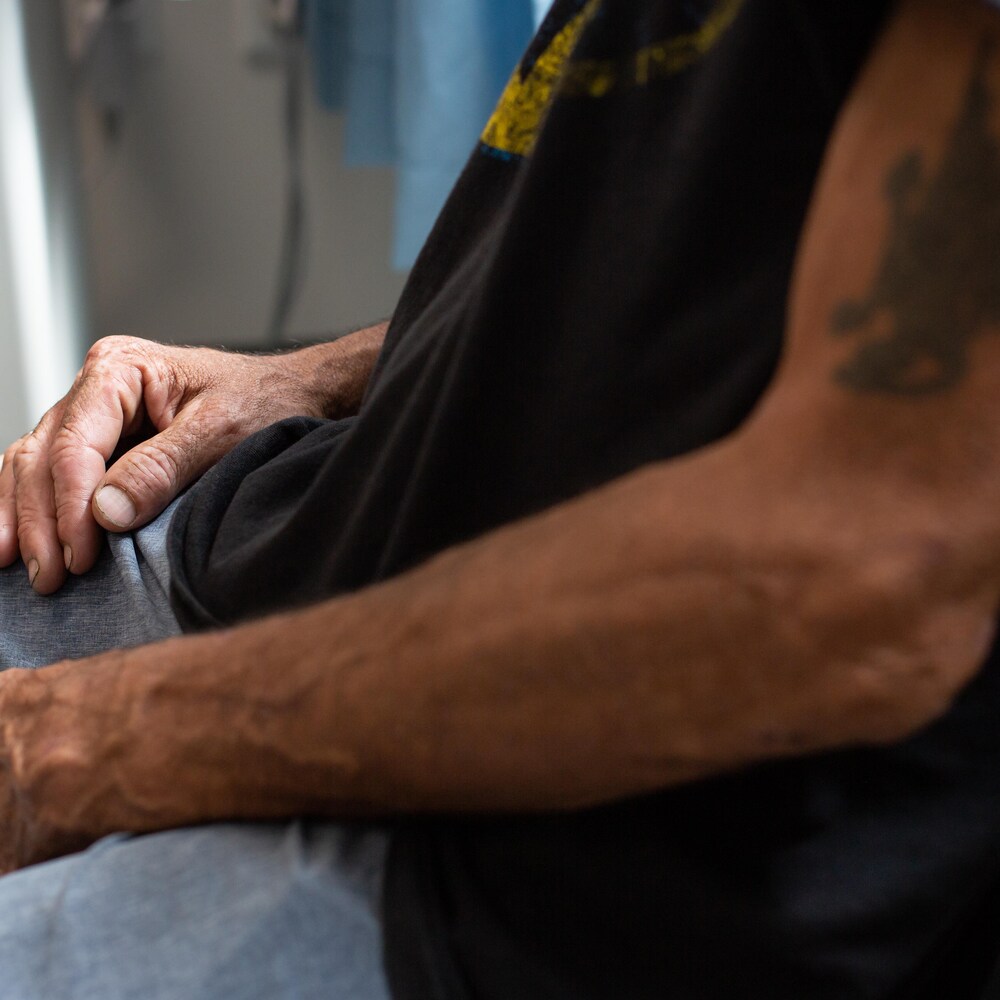 Un homme avec un tatouage au bras a les mains déposées sur ses jambes.