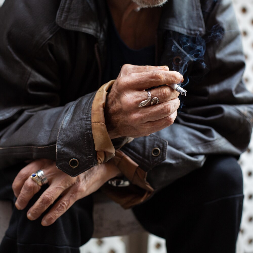 Un homme, assis, fume une cigarette.