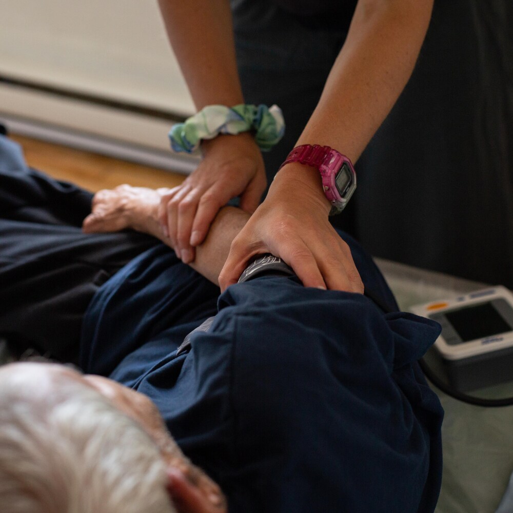 Un homme âgé est allongé sur le côté pendant qu'il est examiné par une médecin.
