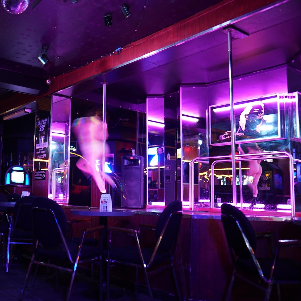 Une danseuse nue floue danse autour d'un poteau sur une scène à l'intérieur d'un bar.