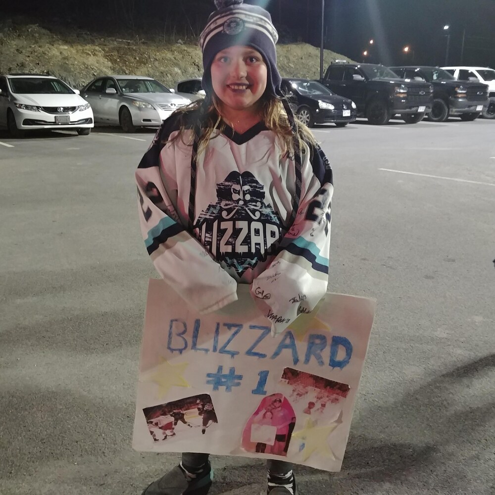 Une jeune femme portant le chandail du Blizzard et une pancarte au nom de l'équipe