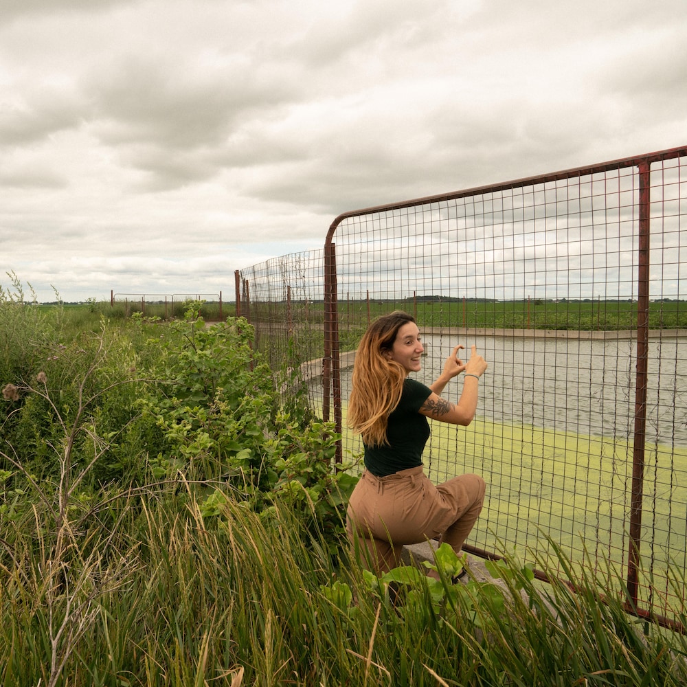 Éliana se tient sur la clôture qui entoure la fosse à purin, entourée d'herbes folles. 