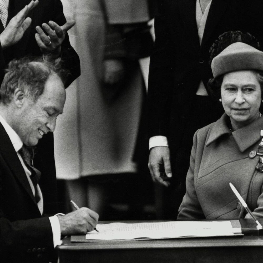 Photo d'archive sur laquelle on voit la reine Élisabeth 2 assise en compagnie de Pierre Elliott Trudeau qui signe proclamation constitutionnelle.