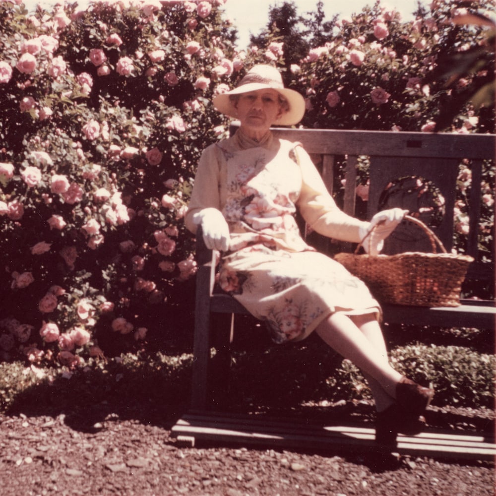 Une femme assise sur un banc entourée de fleurs.