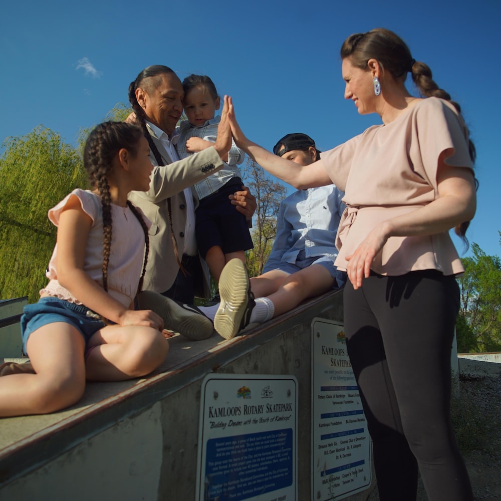 La famille de Bonnie Lépine Antoine est rassemblée, maya et Séquoia sont sur une bordure d'escalier, le père debout tient le plus jeune et Bonnie lui tape dans la main. 