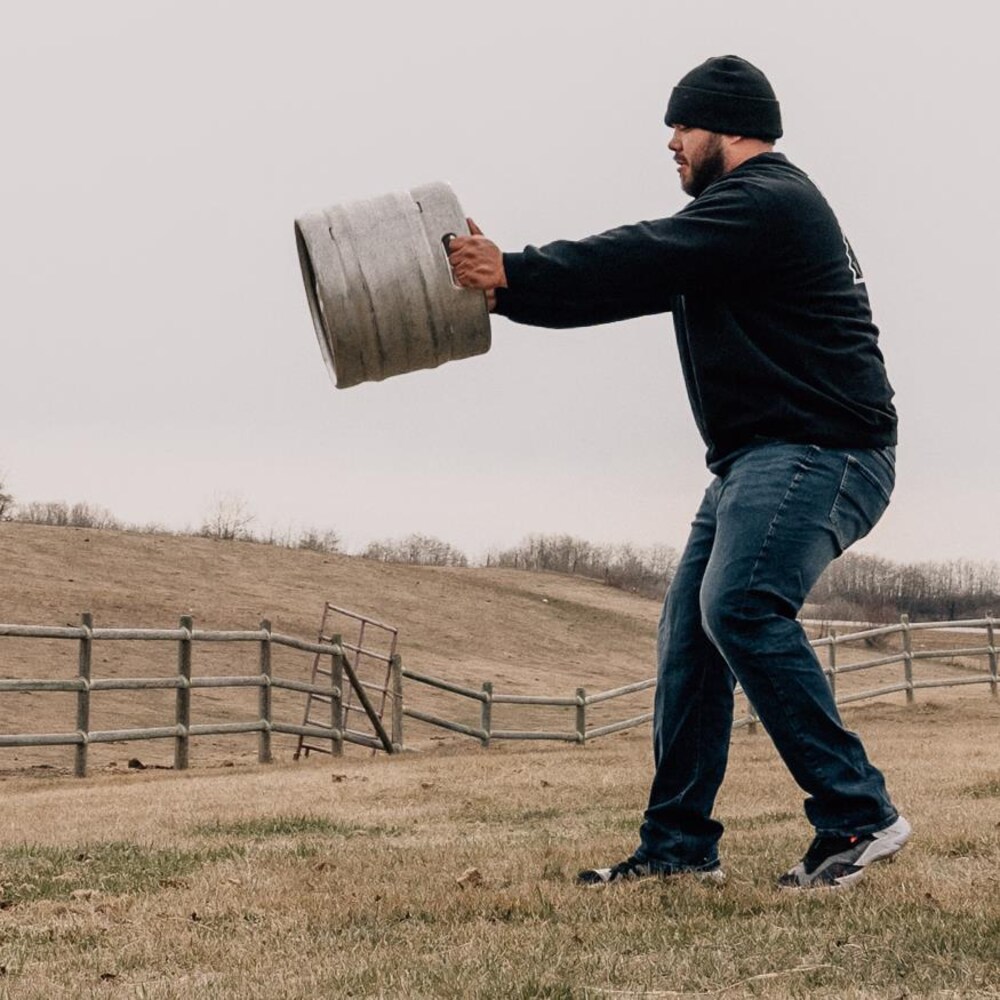 Colten Sloan porte un barile des deux mains qu'il s’apprête à lancer dans les airs sur le site de la ferme familiale. 