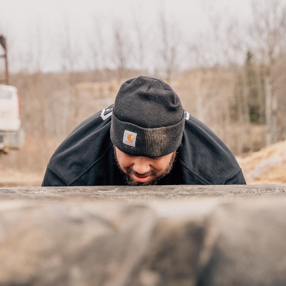 Colten essaye de soulever un pneu de tracteur, il a la tête posée dessus.