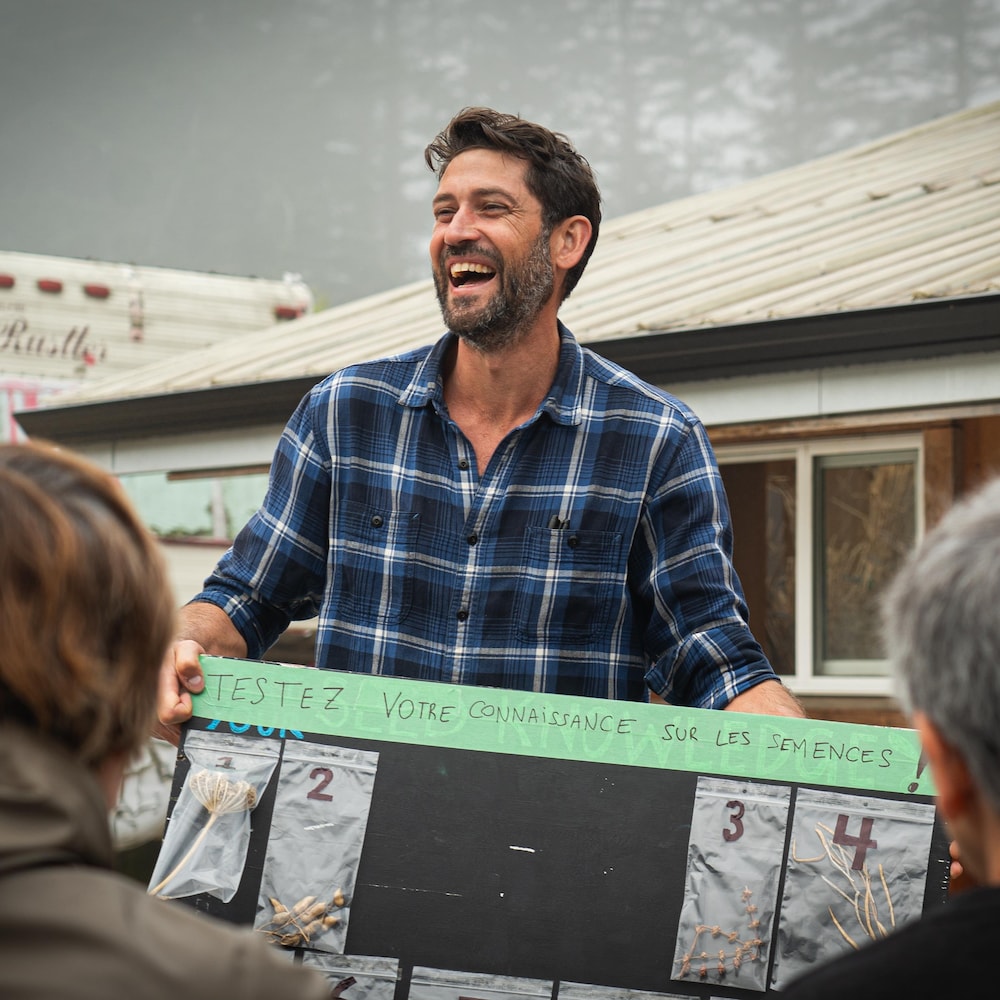 Un bénévole souriant et tenant à la main un carton avec un test de connaissance de semences, à la ferme Metchosin, dans le sud de l'île de Vancouver, en août 2024.
