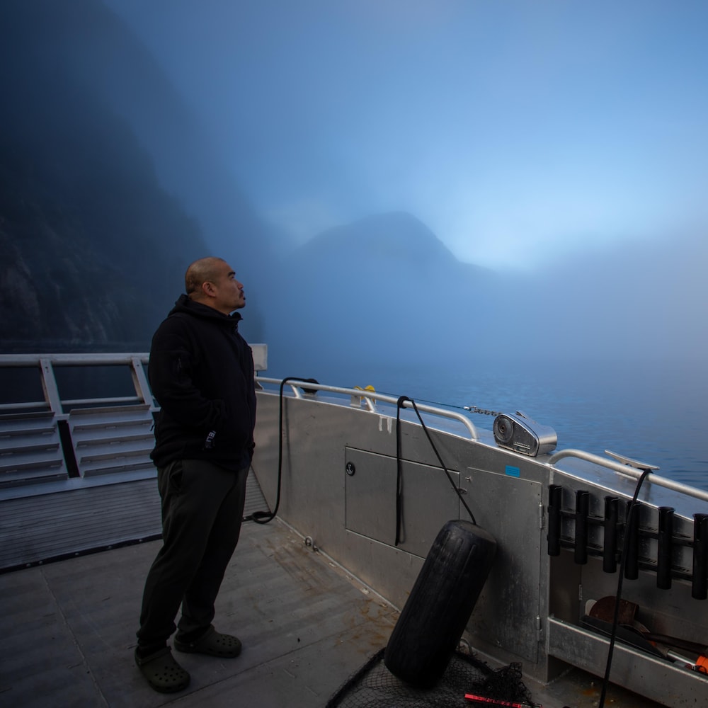 Douglas Neasloss sur le pont d'un bateau dans un fjord embrumé, près de Klemtu, en Colombie-Britannique, en octobre 2023.