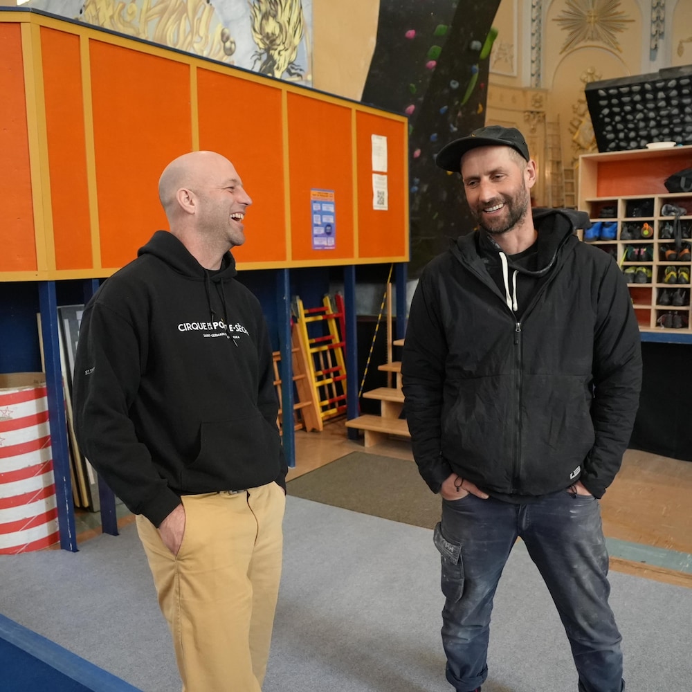 Deux hommes dans la quarantaine riant dans un atelier de cirque au sein d'une église transformée. 
