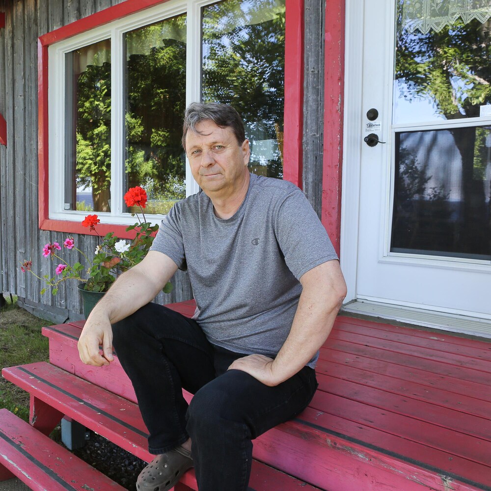 Un homme assis sur les marches de son chalet en bois. 
