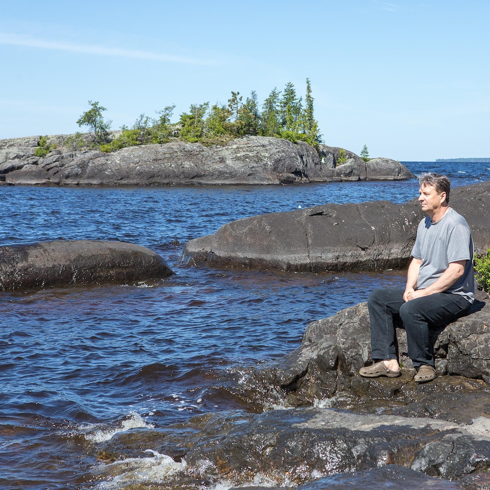 Un homme penseur est assis sur de grosses roches arrondies sur le bord d'un lac. 