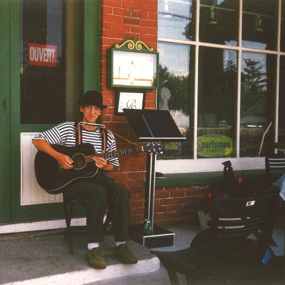 Fred Pellerin joue de l'harmonica et de la guitare sur le perron d'un restaurant.