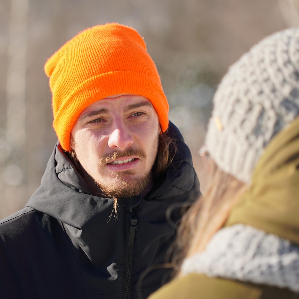 Un jeune homme est en discussion avec une jeune femme de dos. Ils sont à l'extérieur en vêtements d'hiver. 