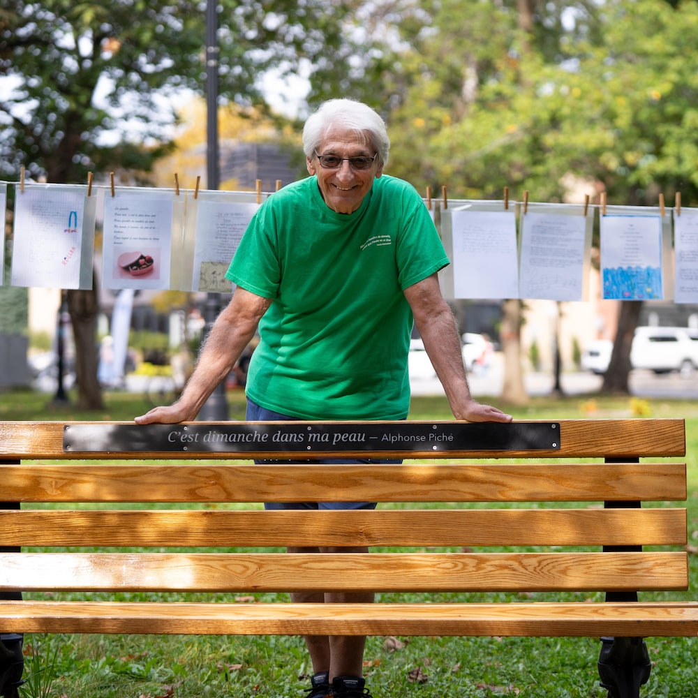 Gaston Bellemare sourit derrière un banc avec l'inscription : c'est dimanche dans ma peau. Signé Alphonse Piché.