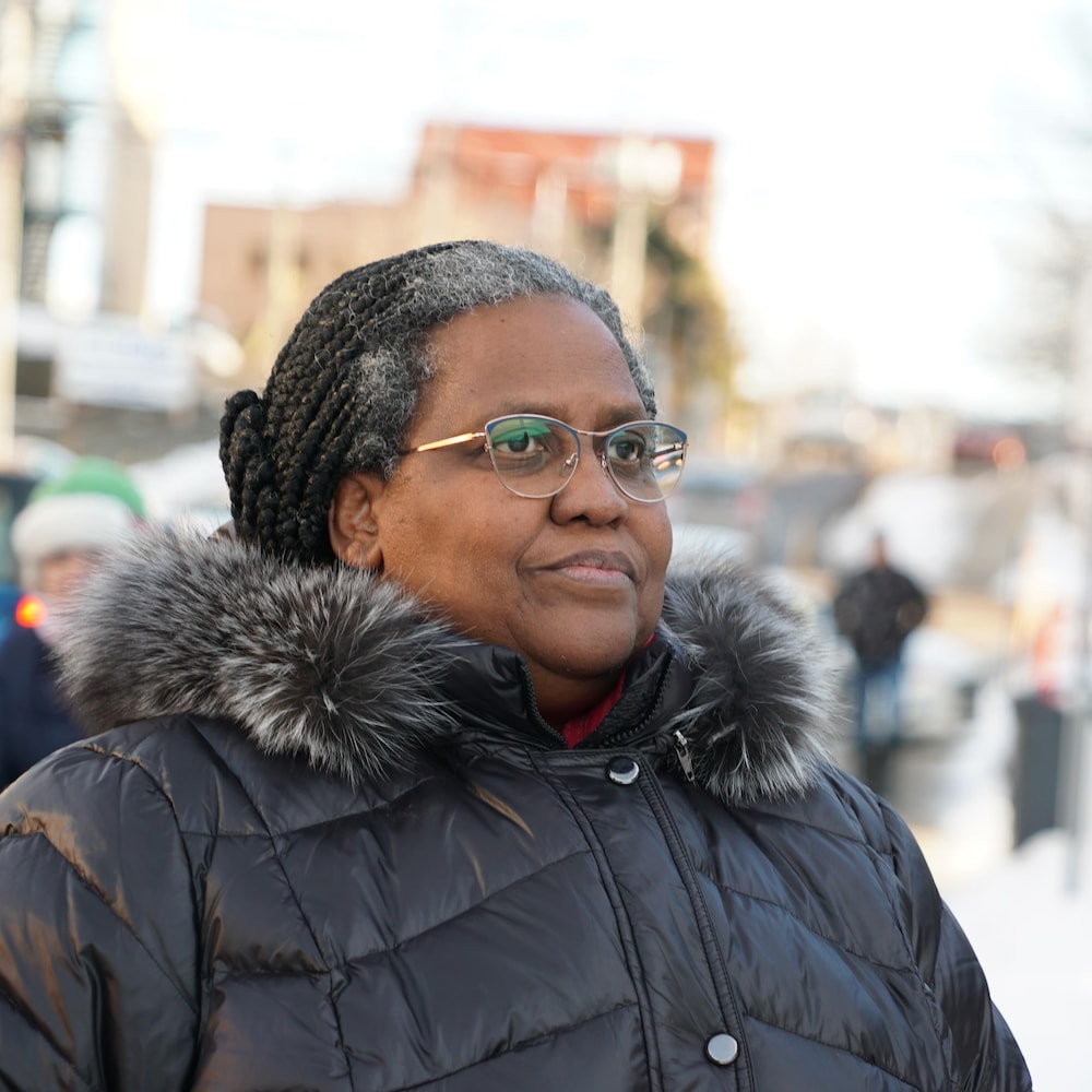 Jeanne-Marie Rugira est à l'extérieur sur une rue où des piétons défilent sur le trottoir, en hiver. 