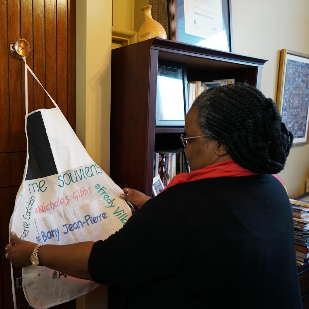 Jeanne-Marie Rugira tient dans ses mains un tablier sur lequel des noms de victimes d'acte de violence policière raciste sont inscrits. 