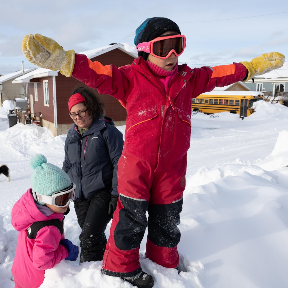 Deux enfants et leur maman jouent sur un banc de neige. 
