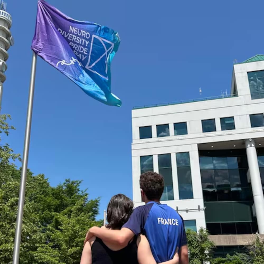 Caroline Jose et son fils Louis sur la place de l'hôtel de ville de Moncton regardant le  drapeau de la fierté de la neurodiversité.