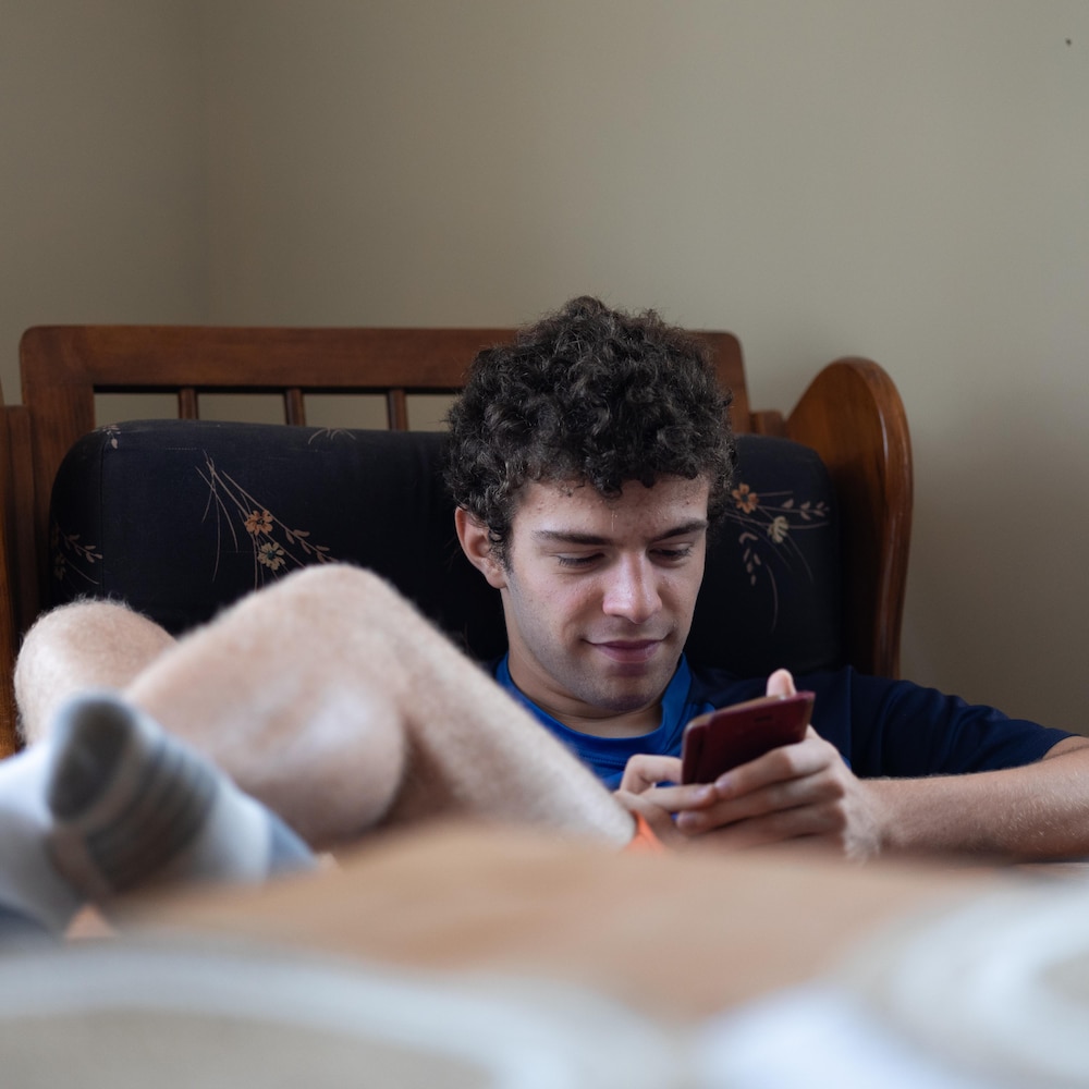 Louis qui joue avec son téléphone assis dans une chaise berssante.