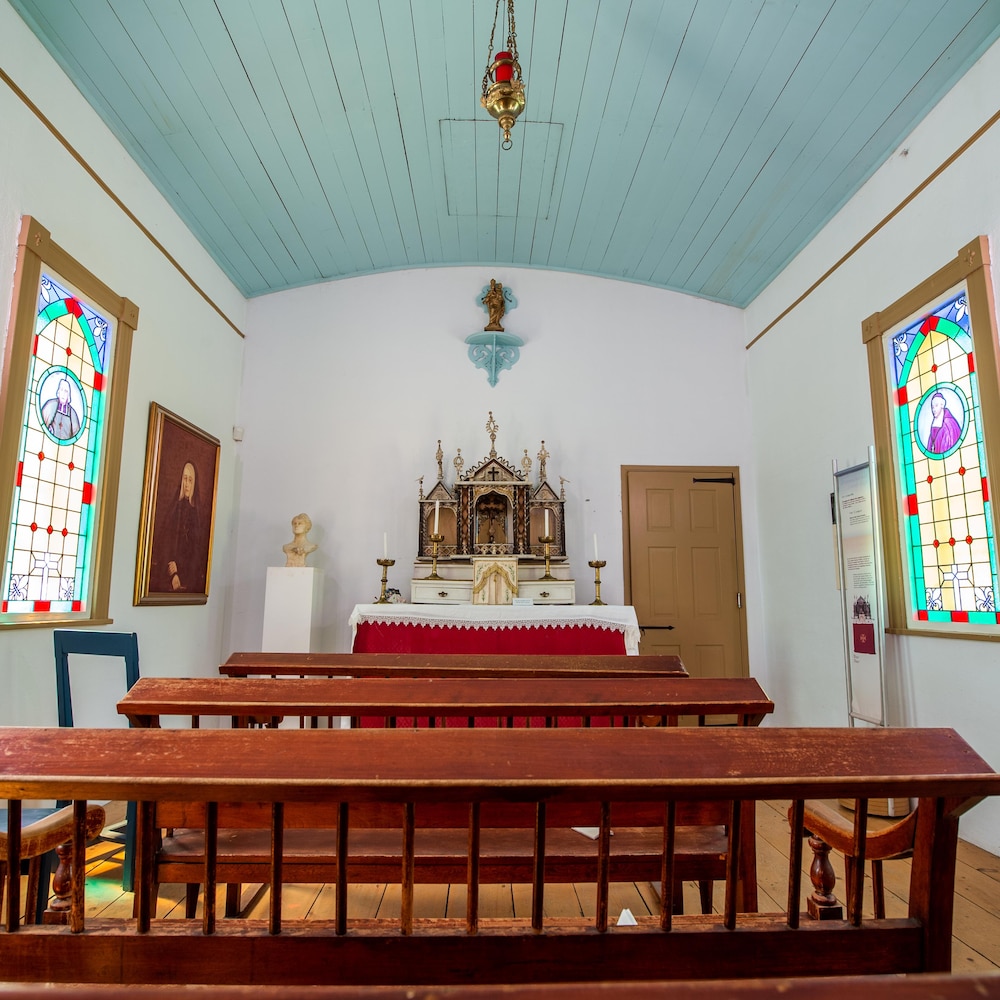 Des bancs d'églises dans un petit espace avec des vitraux et un tabernacle et des cierges à l'avant de la pièce.