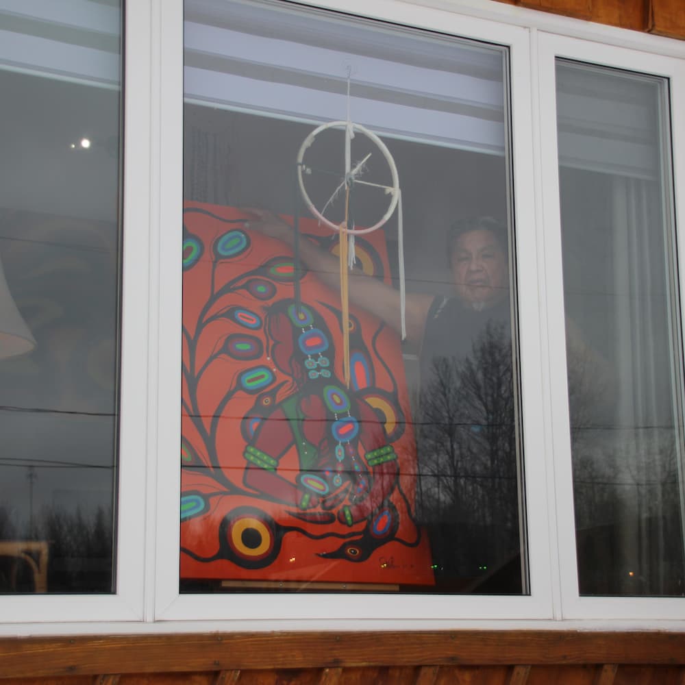 Frank Polson est derrière sa fenêtre et il montre une de ses oeuvres.
