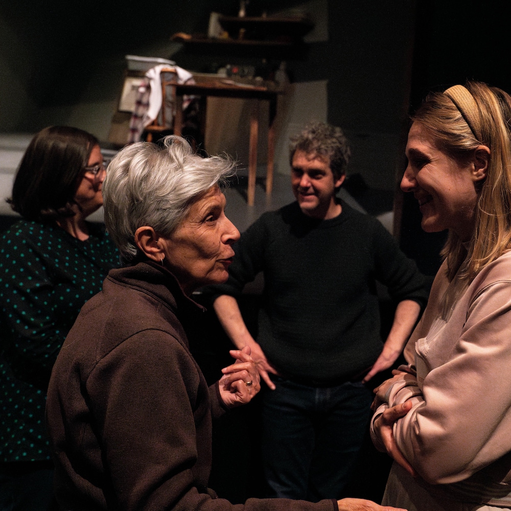Deux femmes discutent ensemble devant une scène de théâtre et un homme et une femme discute derrière elles.