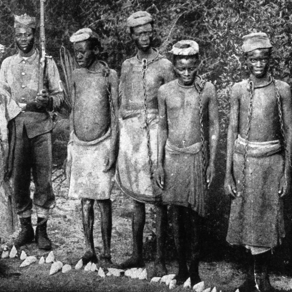 Des esclaves enchaînés en compagnie de ce qui semble être un gardien noir