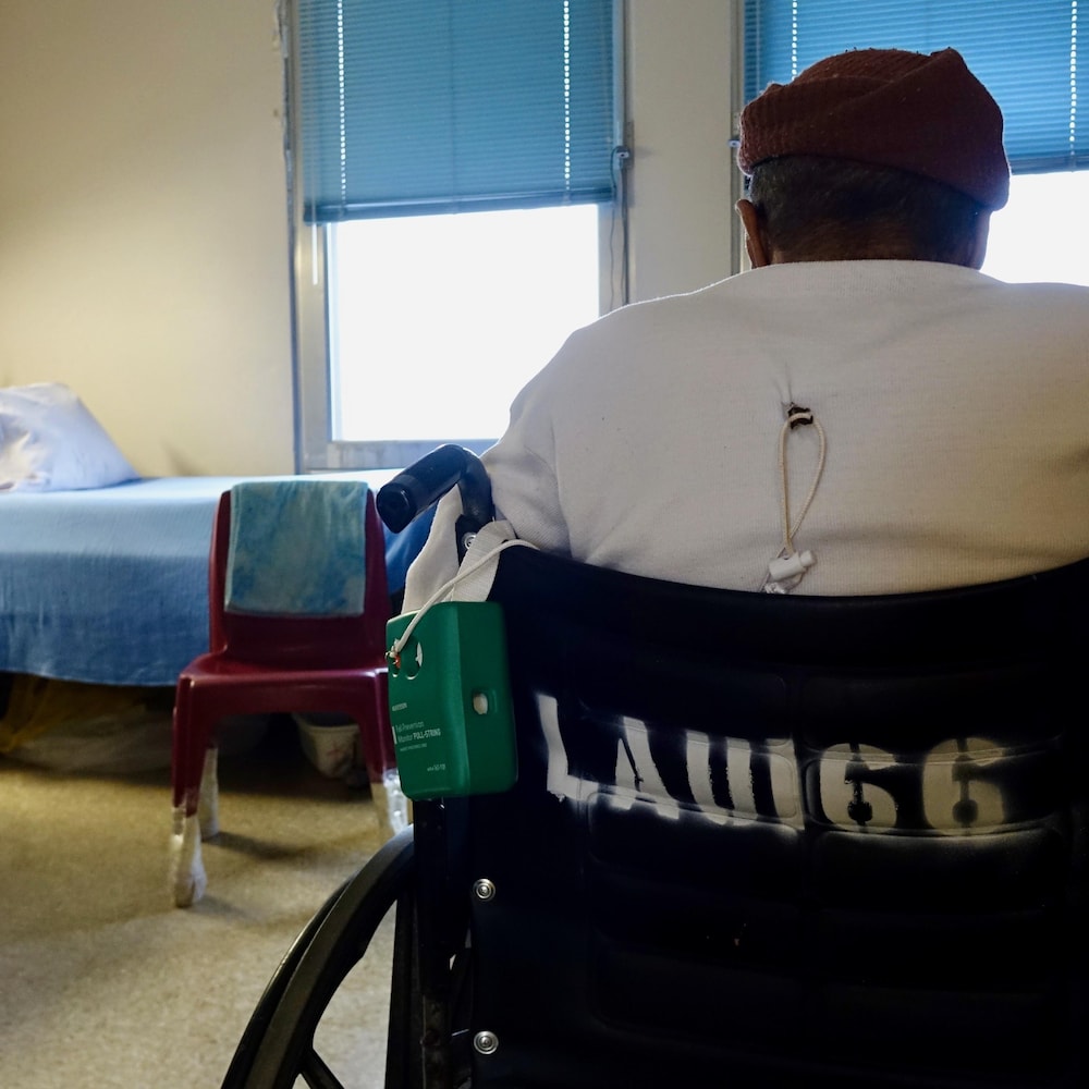 Eugene, un détenu de 73 ans est dans son fauteuil roulant devant deux grandes fenêtres de sa chambre                           