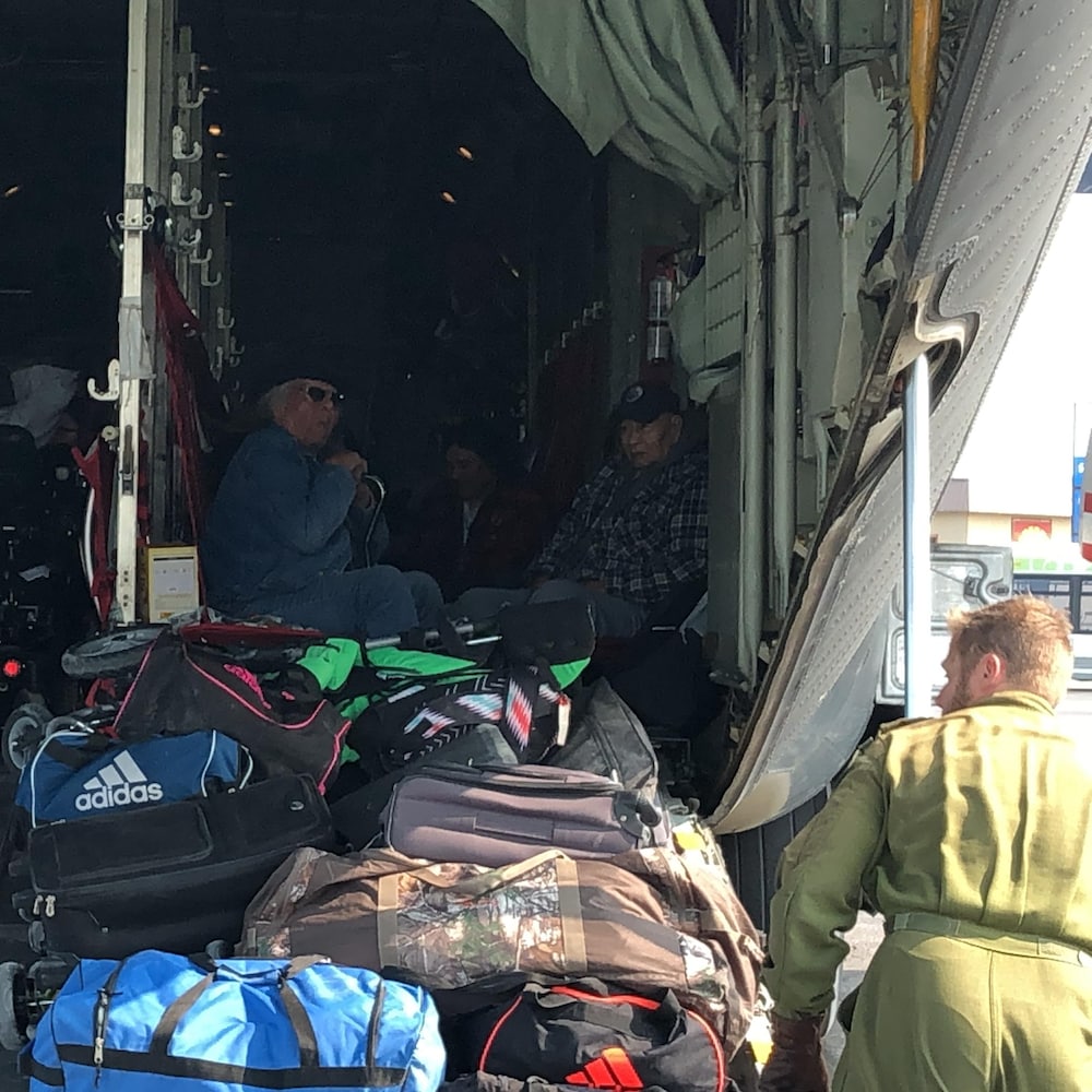 Des personnes sont assises dans un avion qui vient d'atterrir tandis que des militaires s'occupent de décharger des affaires.