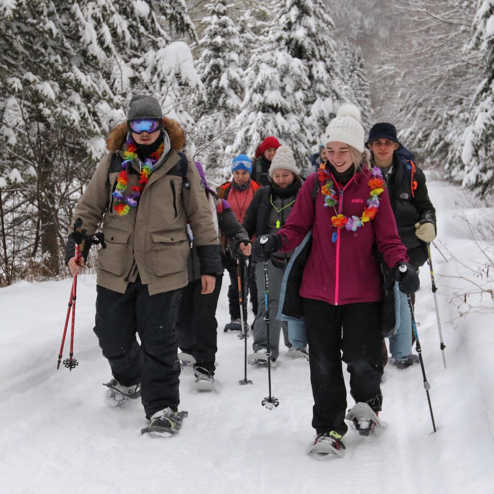 Le groupe de jeunes marche dans la forêt enneigée avec leurs raquettes.