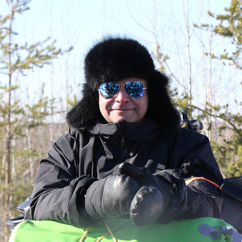 John Paul Murdoch pose les mains sur sa motoneige avec des lunettes de soleil.
