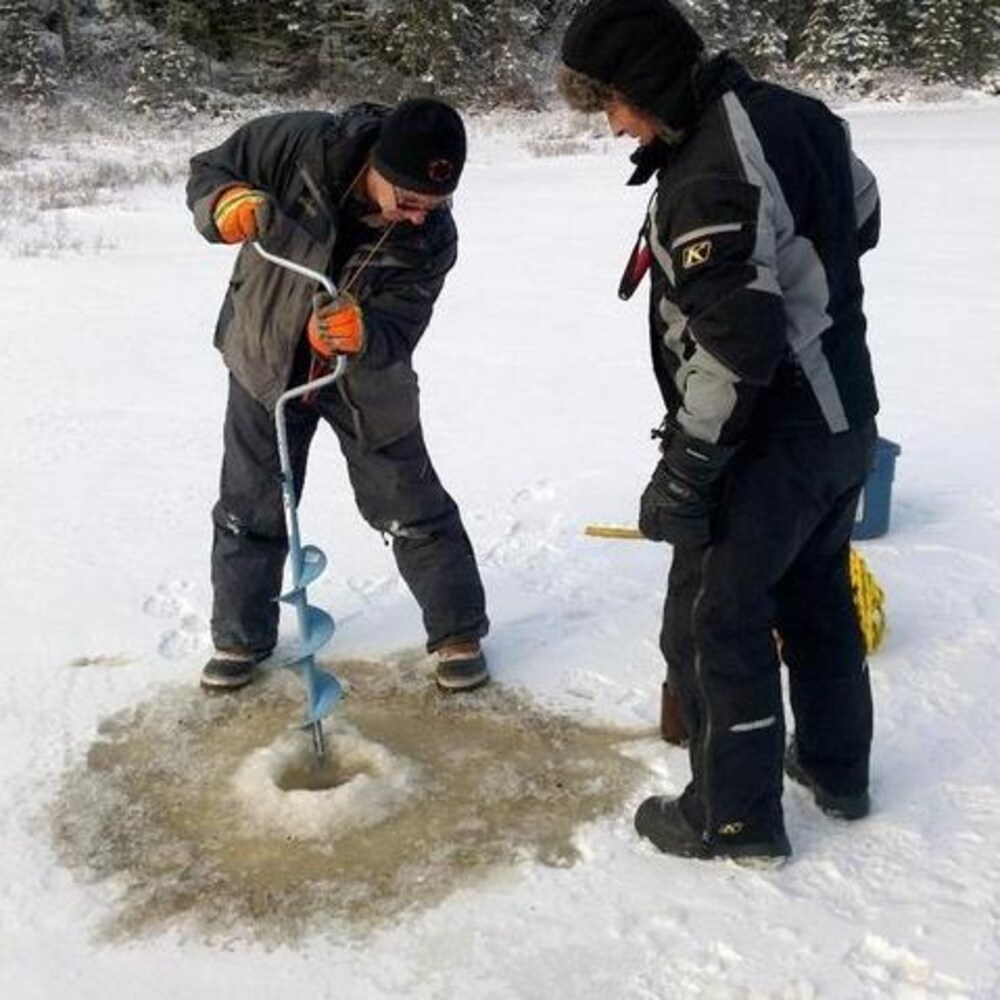 Deux hommes en train de faire un trou dans la glace.