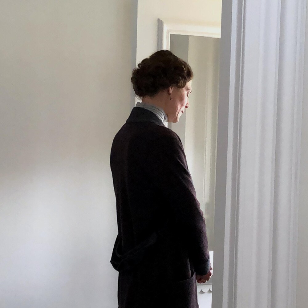 Dans le cadre de porte de l’entrée, la comédienne Hélène Florent reconnecte avec son personnage. Elle a les yeux fermés et la tête légèrement penchée.