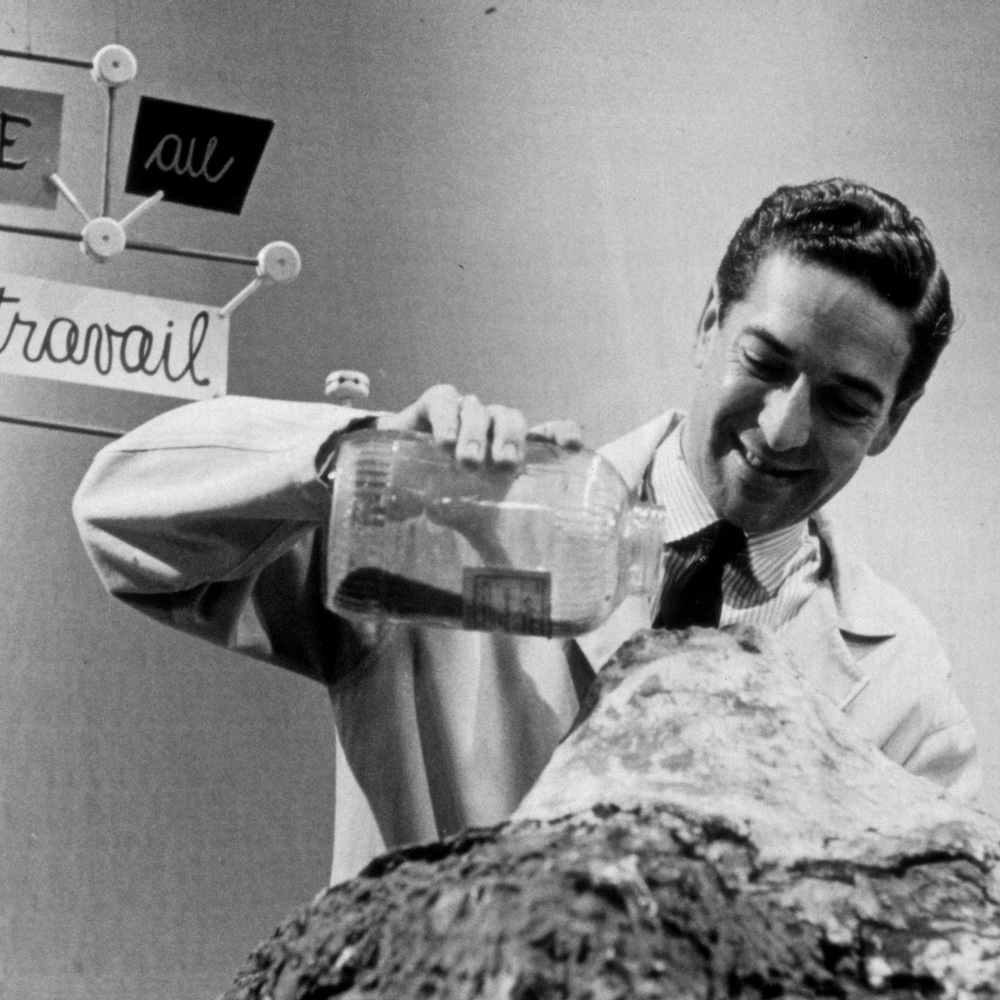 Fernand Seguin qui verse du sable sur une table pour former un volcan.