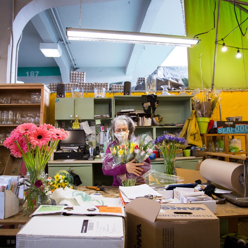Myriam Binette tient plusieurs bouquets de fleurs entre ses bras, derrière son comptoir de travail.
