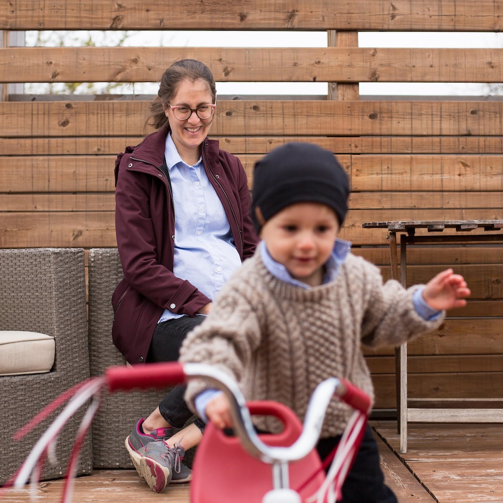 Emily Lavertu observe son fils jouer avec un petit tricycle.