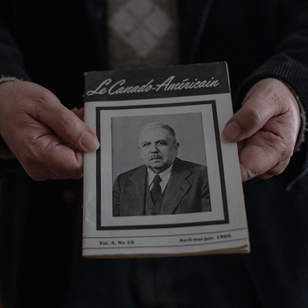 Robert Perreault tient un numéro du magazine « Le Canado-Américain » où figure un portrait de son grand-père Adolphe Robert.