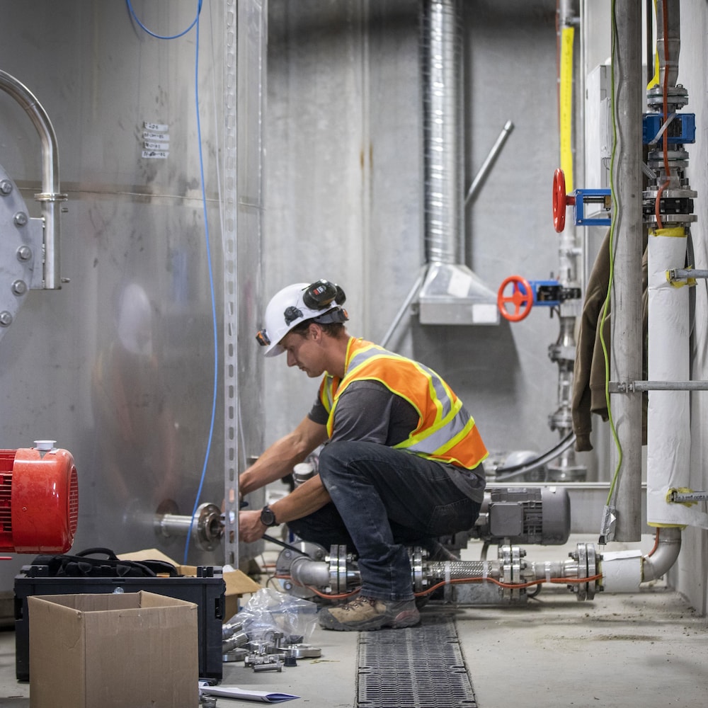 Un ouvrier dans une usine, accroupi près d'un réservoir en métal, en juin 2023, à Chilliwack, en Colombie-Britannique.