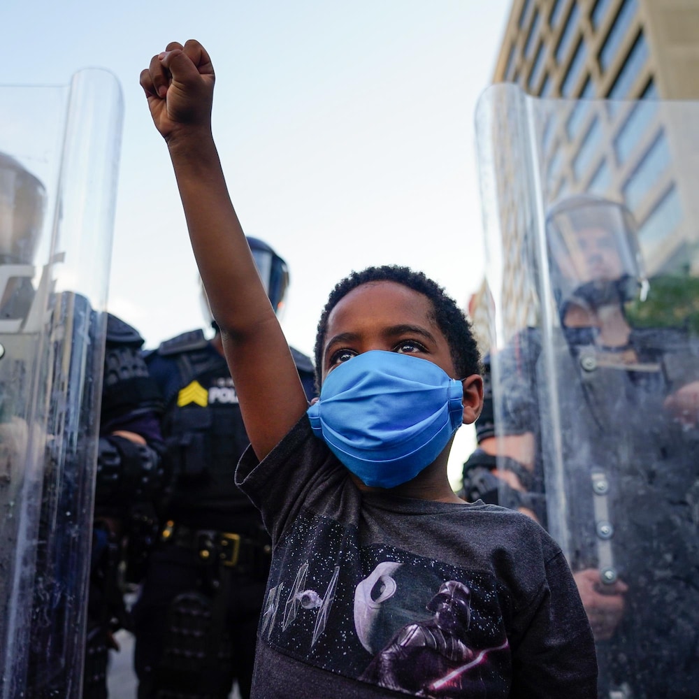 Un garçon lève le poing, devant des policiers protégés par des boucliers.