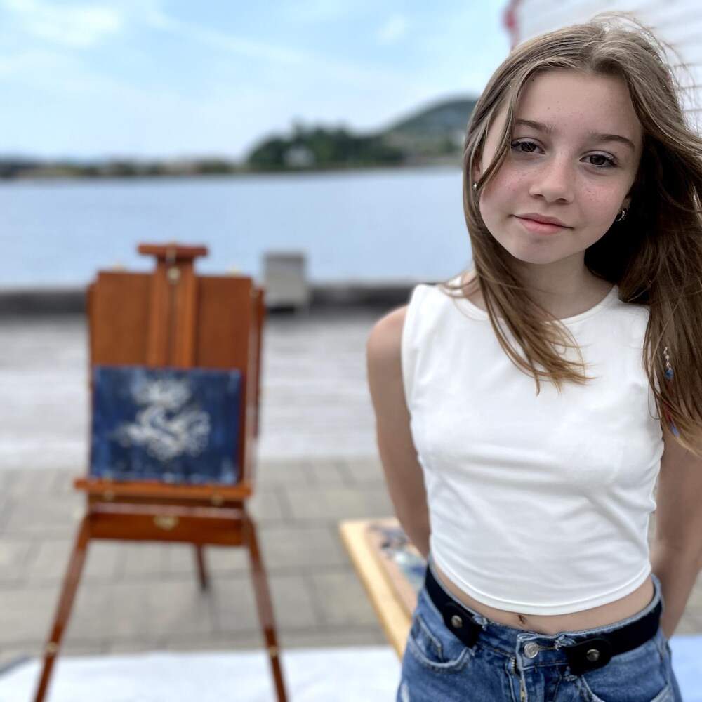 Une jeune peintre et sa toile en arrière plan.