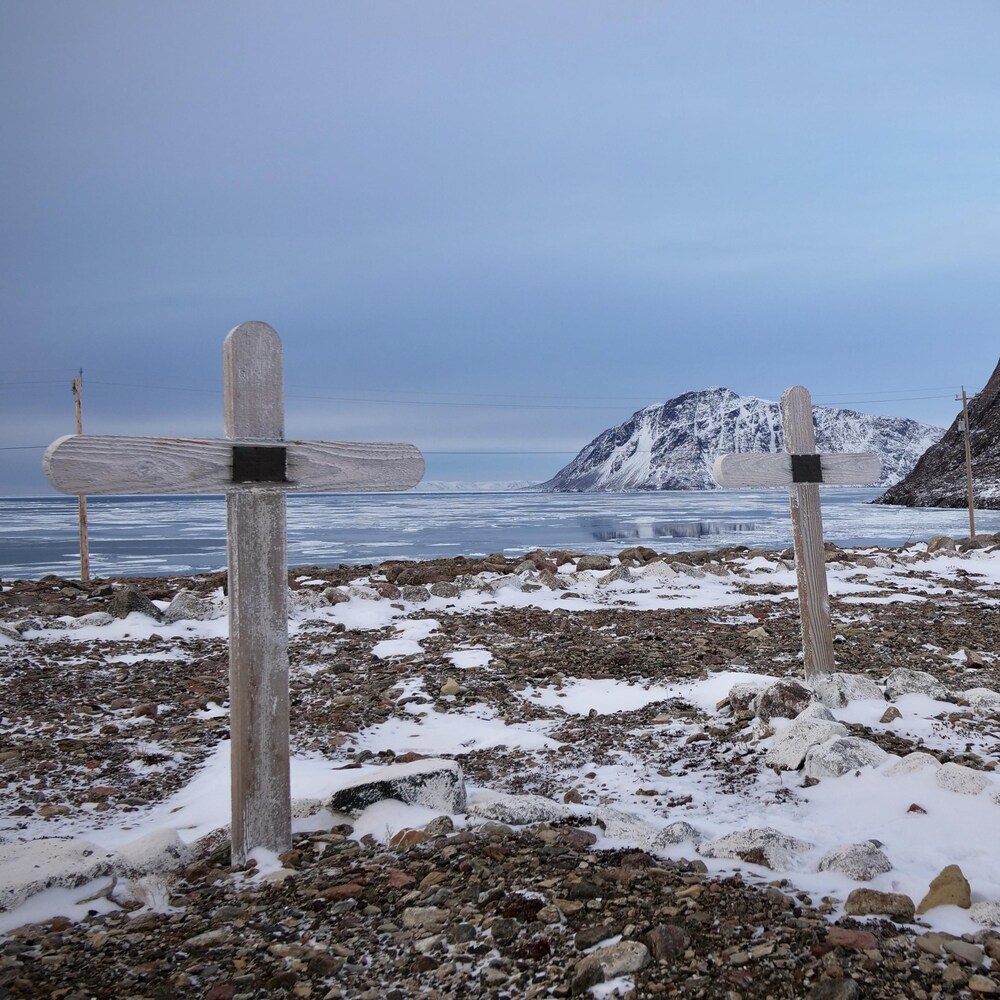 Des croix de bois plantés dans un sol aride et en partie enneigé, près de la rive, dans le cimetière de Grise Fiord.