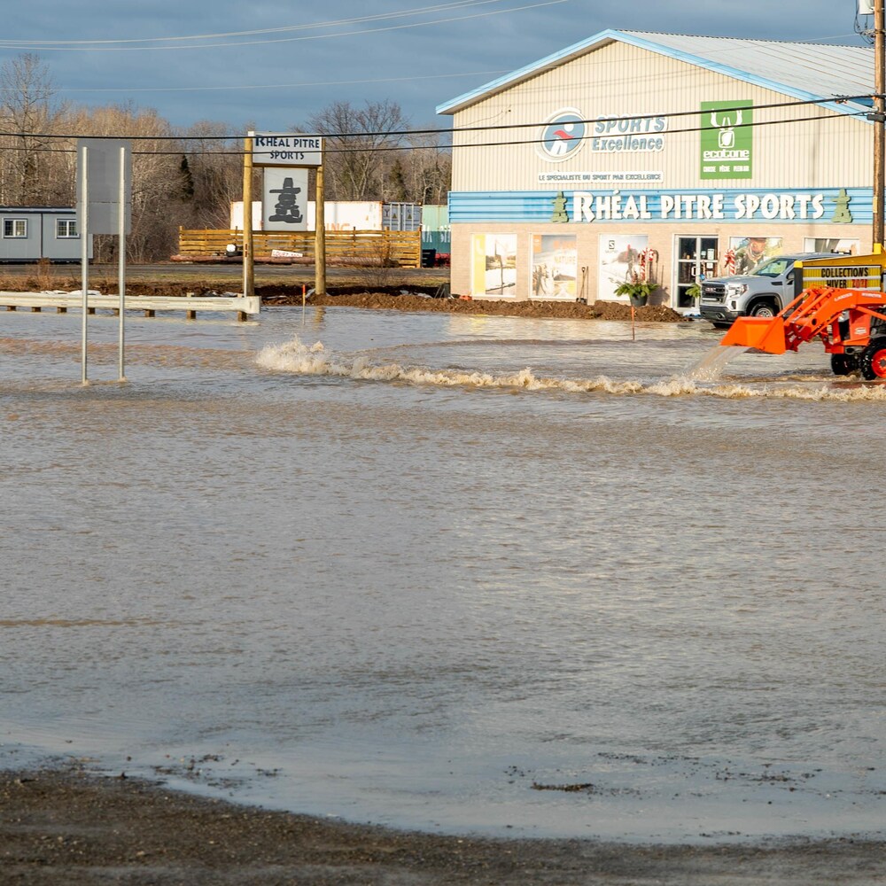Un tracteur repousse l'eau qui recouvre le stationnement d'un magasin de sports.